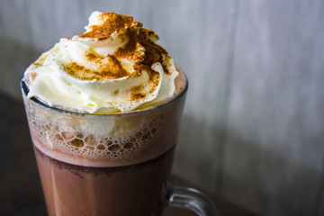 Hot chocolate in a tall glass with whipped cream and cocoa powder