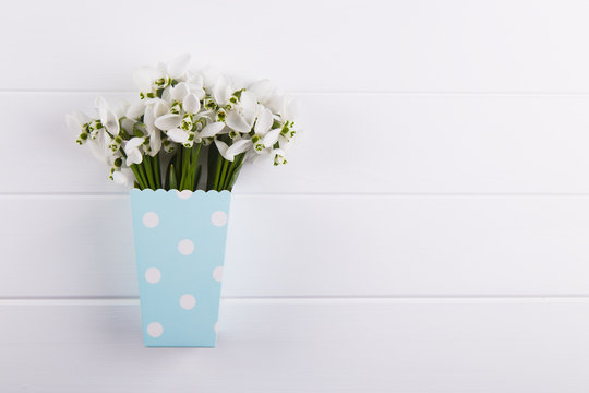 Spring bouquet of snowdrops in paper box on white wooden background
