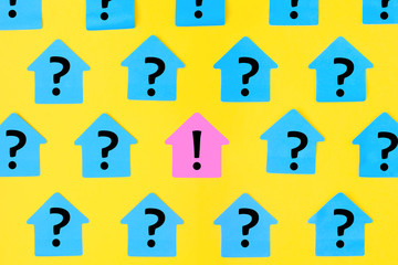 Stickers in the form of houses on a bright yellow background. On blue sticky notes a question mark was written, in the center on a pink paper an exclamation mark.