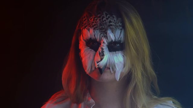 Close-up, Beautiful Girl with Owl Grim on Face Twirls Head in Parties Immune Bird in Smoky Dark Studio