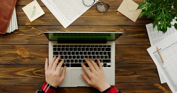 Close up of the female hands with the red plaid sleeves working on the laptop computer with a green screen on the wooden office table with office stuff and plant. Chroma key. Top view