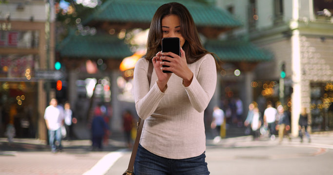 Portrait of cheerful Latina woman taking photo with cellphone in Chinatown