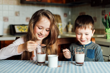Children drink milk in the kitchen at the morning. Sister and brother prepare cocoa and have fun