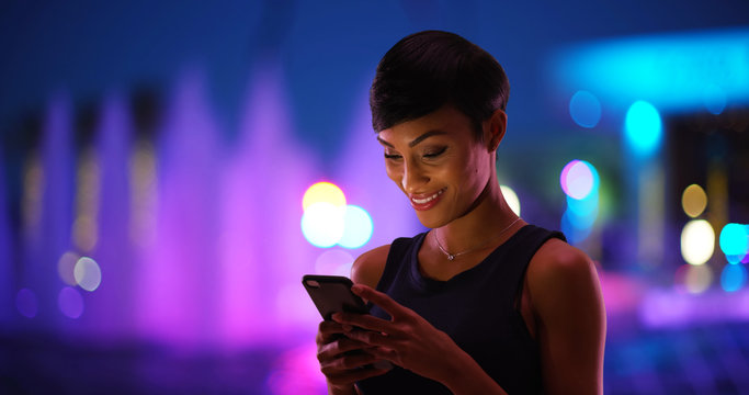 Smiling Young Black Woman Texting On Cell Phone Colorful Fountain In Background