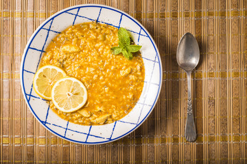 Plate of chicken rice with vegetables and spices presented on a bamboo mat.