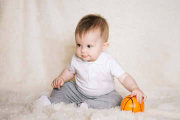 Fototapeta premium Cute young baby sitting on the floor at home and playing with a basketball, sports, healthy and active lifestyle