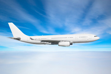 White passenger wide-body aircraft flies at the flight level above the stratus clouds, above it the cirrus against the blue sky.
