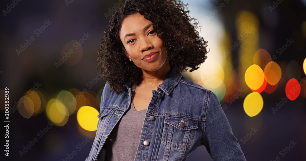 Poster Black girl in her 20s with confident expression posing in city at night