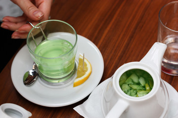 Transparent cup of green tea with lemon on plate on the wooden background