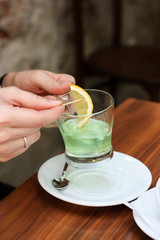 Transparent cup of green tea with lemon on plate on the wooden background