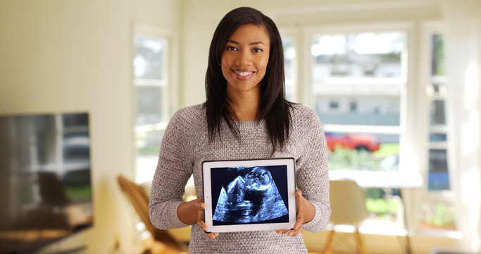 Portrait of joyful black female showing ultrasound picture on computer