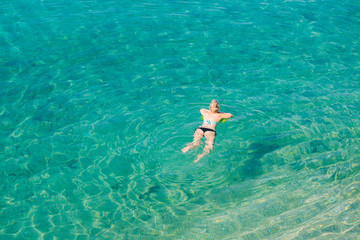 Aerial view of young blonde woman swimming in the transparent turquoise sea. Top view of slim lady relaxing on her holidays.
