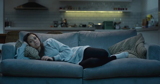 Relaxed woman lying on a sofa in a cozy living room at night watching tv.
