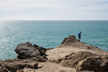 A man standing on a large cliff next to the ocean at Castle Point in New Zealand. 