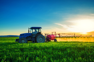 Naklejka premium Farming tractor plowing and spraying on field