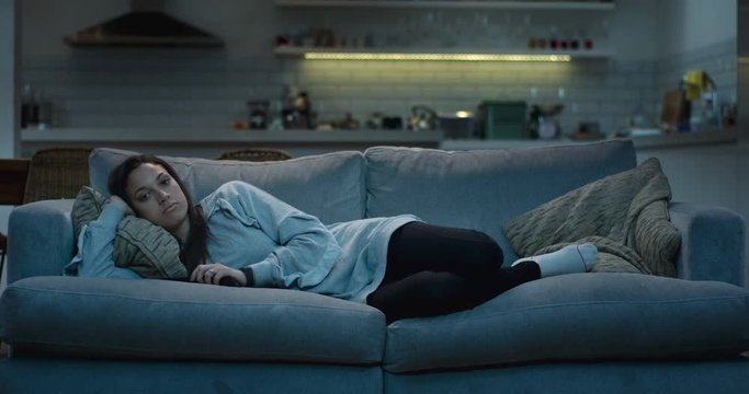 Young woman lying down on a comfy sofa at night watching the television