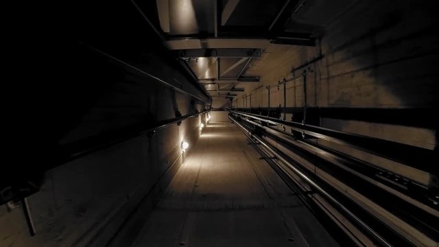 The cabin moves down in an elevator shaft. The view is directed downwards. The camera is moving. The lights in the shaft give the ride its own rhythm.