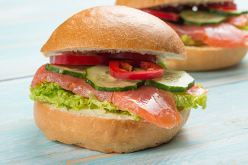 Sandwich with red fish and vegetables, on a blue wooden background.