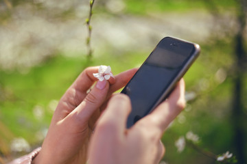 Girl uses her Mobile Phone outdoor, close up. Sunny day. Spring flowers. Beautiful Orchard.