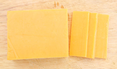 Cheddar cheese slices on wooden background.