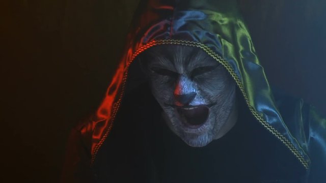 Close-up, Guy with Wolf Wolf on Face in Black Hood Imitates Animal Roar in Smoky Studio