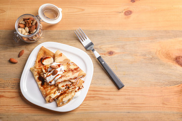 Thin pancakes served with chocolate syrup, cream and banana on plate, top view