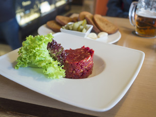 close up fresh Steak tartare with lettuce leaves on white plate, toasted bread, garlick, pickles and beer in  background, selective focus
