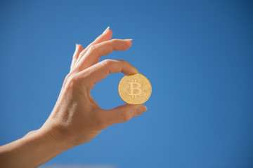 Plakat Hand holding golden bitcoin coin on blue sky background