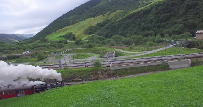 Steam train leaves the town of Realp in summer. Gliding drone shot.