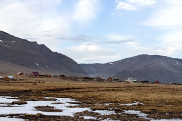 A rural landscape with houses and cows on the shore of Lake Baikal in early spring on a mountain background in a sunny clear day.