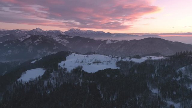 Aerial view flying over winter landscape with colorful sunrise in Slovenia.