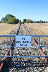 a black and white No Unauthorised Access warning sign on the fence of a disused railway line