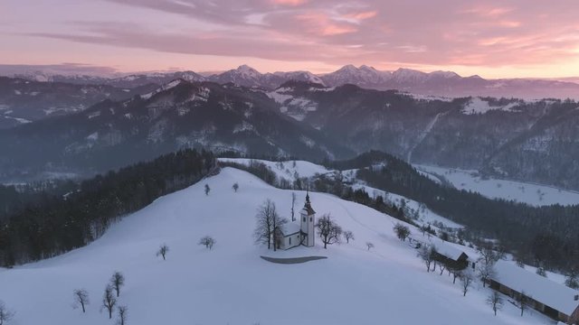 Aerial view flying over Jamnik Church in winter landscape with colorful sunrise in Kranj, Slovenia.