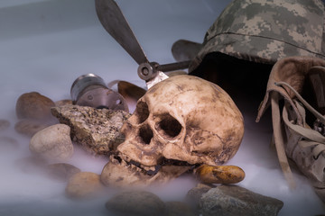 Corpses in military uniform on ice smoke. The human skull is next to the military cap and boots.