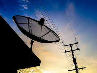 Silhouette of satellite dish and electrical post in the sunrise sky.