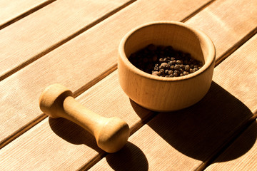 Mortar with black pepper and pestle .  On wooden background