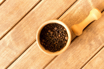 Mortar with black pepper and pestle .  On wooden background