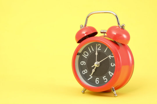 Red vintage alarm clock on yellow background.