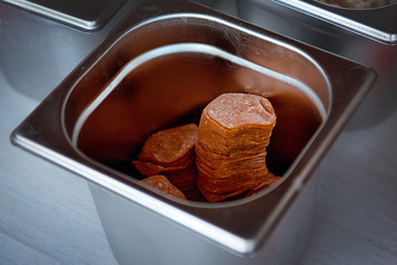 Sliced pepperoni sausage in an iron container on a table.