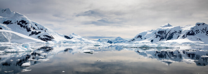 Fototapeta na wymiar Snow covered mountains reflected on still water with cloudy sky, Paradise Habour, Antarctica