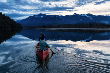 Adventurous people on a wooden canoe are enjoying the beautiful Canadian Mountain Landscape during a vibrant sunset. Taken in Harrison River, East of Vancouver, British Columbia, Canada.