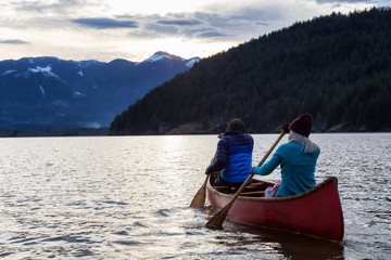 Fototapeta na wymiar Adventurous people on a wooden canoe are enjoying the beautiful Canadian Mountain Landscape during a vibrant sunset. Taken in Harrison River, East of Vancouver, British Columbia, Canada.