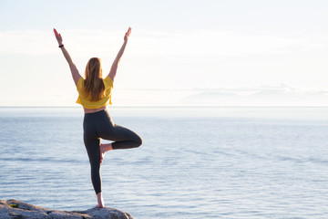 Young woman practicing yoga on a rocky island during a vibrant sunset. Taken in Whytecliff Park, Horseshoe Bay, West Vancouver, British Columbia, Canada.