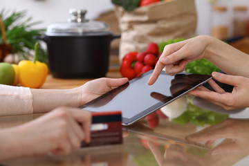 Closeup of human hands cooking in kitchen. Women discuss a menu using tablet computer. Copy space area at touch pad. Healthy meal, vegetarian food and lifestyle concepts