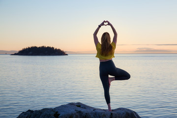 Young woman practicing yoga on a rocky island during a vibrant sunset. Taken in Whytecliff Park,...