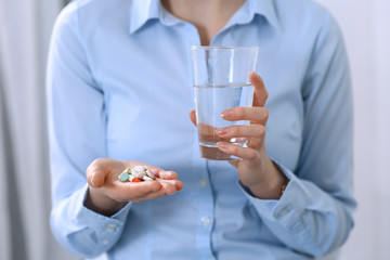 Young unknown woman holding pills and glass of water, closeup of hands.  Medicine and healthcare concept