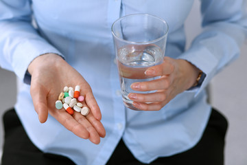Young unknown woman holding pills and glass of water, closeup of hands.  Medicine and healthcare concept