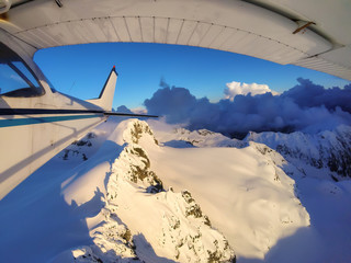 Fototapeta premium Small airplane flying over the Canadian Mountain Landscape during a vibrant sunset. Taken near Squamish, North of Vancouver, British Columbia, Canada.