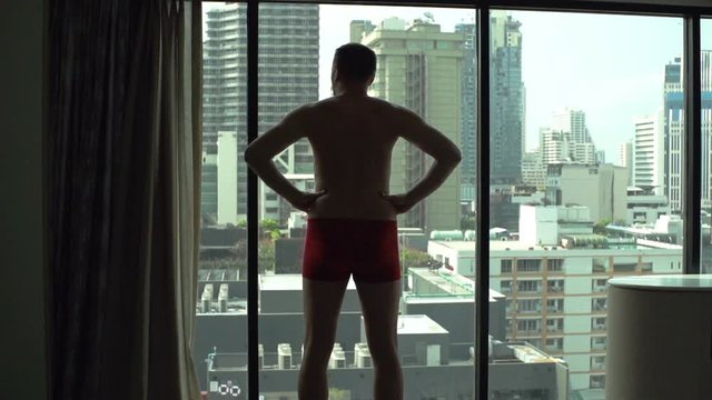 Man wearing only underwear and admiring the view from the window, slow motion shot at 120fps
