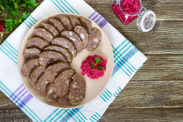Home made dietary sausage from the liver on a wooden table. Sausage cut into pieces on a plate with horseradish sauce. Top view.